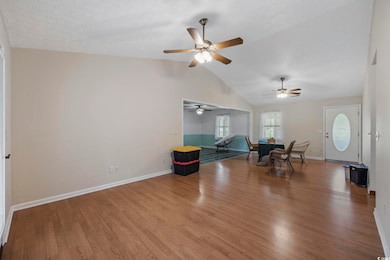 Living area with wood finished floors, a ceiling fan, baseboards, vaulted ceiling, and a textured ceiling