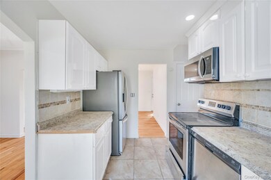 Kitchen with stainless steel appliances, tasteful backsplash, light countertops, white cabinetry, and light wood-style floors