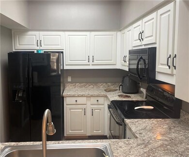 Kitchen with black appliances, white cabinetry, and light laminate counters