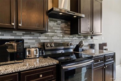 Kitchen, stainless steel electric stove, dark brown cabinetry, light stone countertops, and backsplash