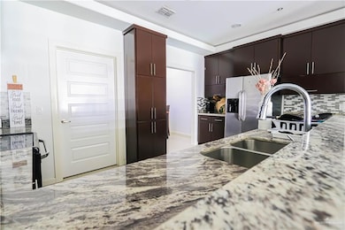 Kitchen with light stone counters, visible vents, backsplash, a sink, and stainless steel fridge