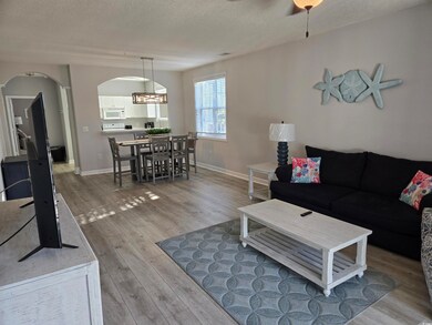 Living room with a textured ceiling, light wood-style flooring, arched walkways, and ceiling fan