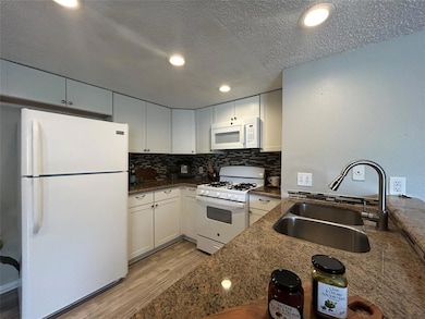 Kitchen with white appliances, a sink, light wood
