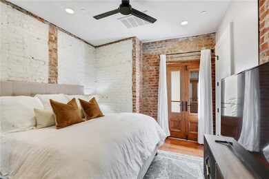 Large bedroom with French Doors for air, a ceiling fan, and exposed brick throughout.