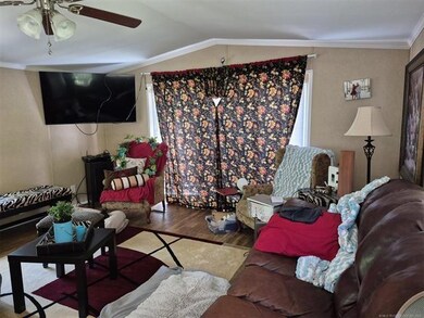 Living room with wood finished floors, ceiling fan, ornamental molding, and vaulted ceiling