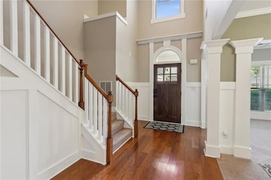 Foyer entrance featuring wood-type flooring, a high ceiling, stairs, decorative columns, and a wainscoted wall