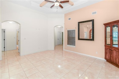 Spare room featuring a towering ceiling, arched walkways, a ceiling fan, ornamental molding, and light tile patterned flooring
