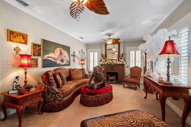 Living room with carpet flooring, a brick fireplace, ceiling fan, and crown molding
