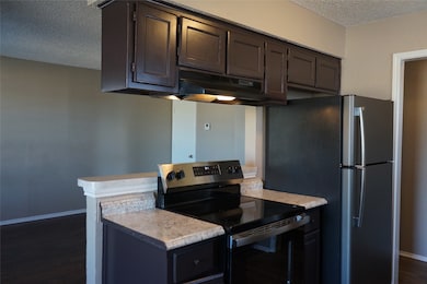Kitchen with a textured ceiling, appliances with stainless steel finishes, dark wood-style flooring, under cabinet range hood, and dark brown cabinetry