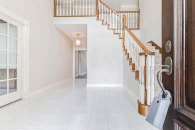 Step through the entryway into a soaring grand foyer, where a sweeping staircase draws the eye upward and sets a dramatic first impression. A soft, neutral palette and elegant tile flooring enhance the home’s timeless allure.