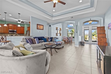 Living area featuring ceiling fan, french doors, light tile patterned floors, a tray ceiling, and arched walkways