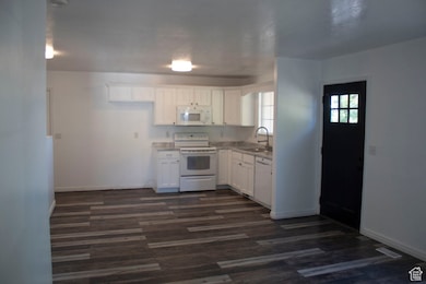Kitchen with white appliances, white cabinetry, dark wood-style floors, and light countertops
