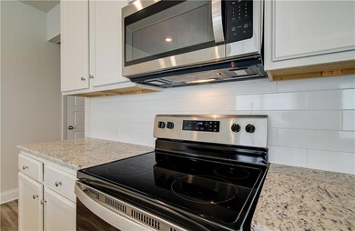 Kitchen featuring appliances with stainless steel finishes, white cabinetry, light stone countertops, and tasteful backsplash