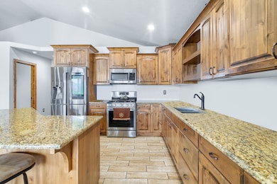 Kitchen featuring stainless steel appliances, a sink, vaulted ceiling, light stone counters, and open shelves