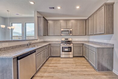 The kitchen is equipped with stainless steel appliances such as a gas range, built-in microwave, and dishwasher. Overhead recessed lighting provides ample illumination throughout the space. Additionally, numerous outlets along the walls ensure convenient access to power for various kitchen appliances and devices.