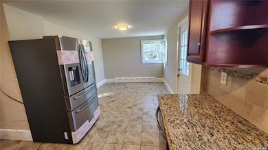 Kitchen with stainless steel refrigerator with ice dispenser, dark stone counters, baseboard heating, decorative backsplash, and open shelves