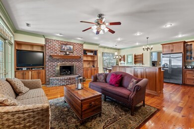 Living room with heart-pine flooring, fireplace with gas logs, crown molding, and ceiling fan with notable chandelier