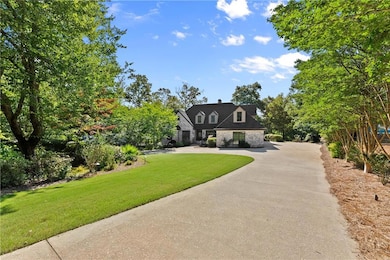 Cape cod-style house with a front yard, curved driveway, a chimney, and stone siding