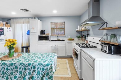 Kitchen with open shelves, white appliances, wall chimney exhaust hood, white cabinetry, and light tile patterned flooring