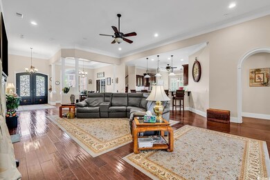 Living room with a chandelier, ceiling fan, plenty of natural light, dark wood-style floors, and crown molding