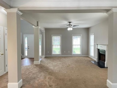 Unfurnished living room with carpet, decorative columns, a fireplace with flush hearth, and a ceiling fan