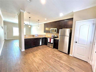 Kitchen featuring dark brown cabinets, appliances with stainless steel finishes, decorative light fixtures, ornamental molding, and backsplash
