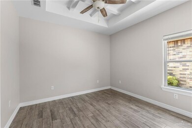 Empty room featuring ceiling fan, wood finished floors, baseboards, and a tray ceiling