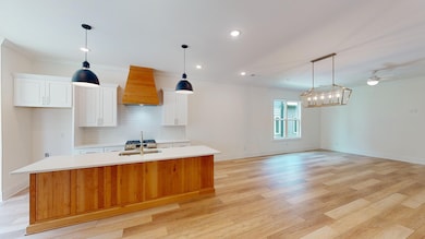 Kitchen with premium range hood, an island with sink, light countertops, a sink, and decorative backsplash