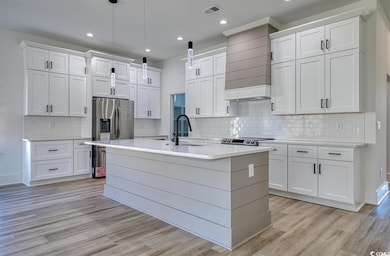 Kitchen with light wood-style flooring, decorative backsplash, white cabinetry, light countertops, and an island with sink