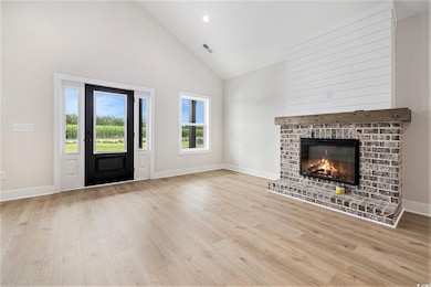 Unfurnished living room with high vaulted ceiling, wood finished floors, a brick fireplace, and baseboards
