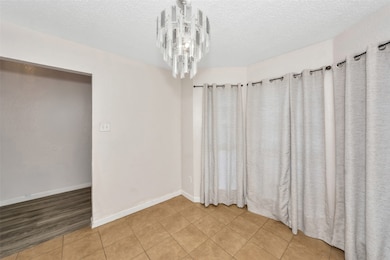 Tiled empty room with a textured ceiling and a chandelier