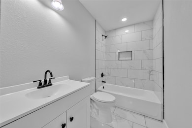 Full bath featuring vanity, a textured wall, tub / shower combination, marble look tiles, and recessed lighting