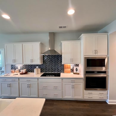 Kitchen featuring appliances with stainless steel finishes, wall chimney range hood, white cabinetry, light countertops, and tasteful backsplash