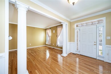 Foyer entrance with ornate columns, a wainscoted wall, light wood finished floors, and crown molding