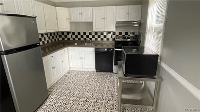 Kitchen with vinyl  tile floors, plenty of countertops, backsplash, white cabinetry, black dishwasher, and stainless steel fridge