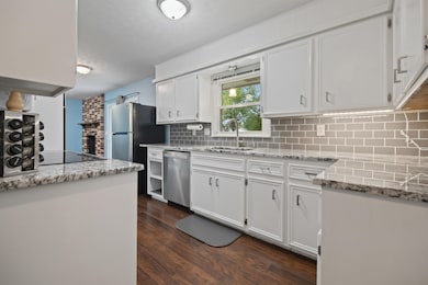 Kitchen featuring white cabinets, light stone countertops, dark wood-style floors, appliances with stainless steel finishes, and backsplash