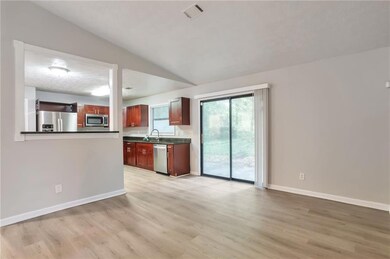 Kitchen with appliances with stainless steel finishes, dark countertops, light wood finished floors, and vaulted ceiling