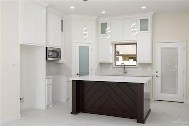 Kitchen with a kitchen island, light marble finish floors, white cabinetry, stainless steel microwave, and recessed lighting