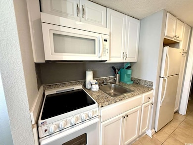 Kitchen with white appliances, white cabinetry, light tile patterned floors, a textured ceiling, and a textured wall