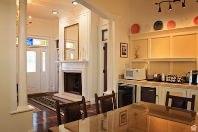 Kitchen with beverage cooler, dark wood-style flooring, white microwave, crown molding, and decorative columns
