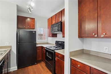 Kitchen with wood finished floors, a sink, black appliances, light countertops, and reddish brown cabinets
