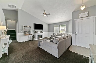 Living area with a ceiling fan, lofted ceiling, a lit fireplace, a wainscoted wall, and stairway