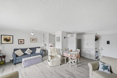 Living area with a textured ceiling, light wood-style flooring, and ceiling fan