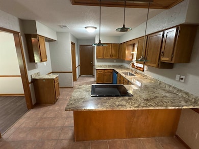 Kitchen featuring a textured wall, brown cabinets, a peninsula, a textured ceiling, and decorative light fixtures