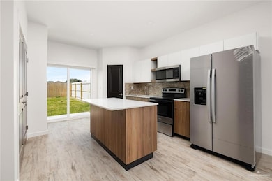 Kitchen featuring appliances with stainless steel finishes, a kitchen island, white cabinetry, light countertops, and backsplash