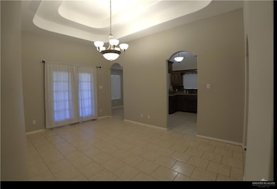 Spare room with arched walkways, a raised ceiling, light tile patterned floors, and a chandelier