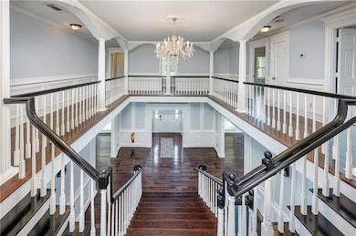 Stairs with ornamental molding, a decorative wall, hardwood / wood-style floors, a chandelier, and a wainscoted wall