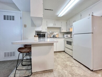 Kitchen with white appliances, white cabinetry, light countertops, a textured ceiling, and a breakfast bar area