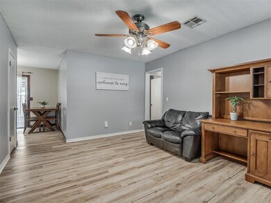 Living room with light wood finished floors, ceiling fan, baseboards, and a textured ceiling