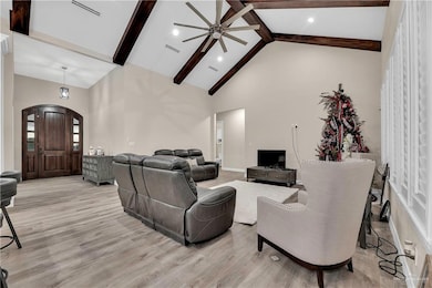 Living room featuring high vaulted ceiling, light wood-style flooring, visible vents, and beamed ceiling